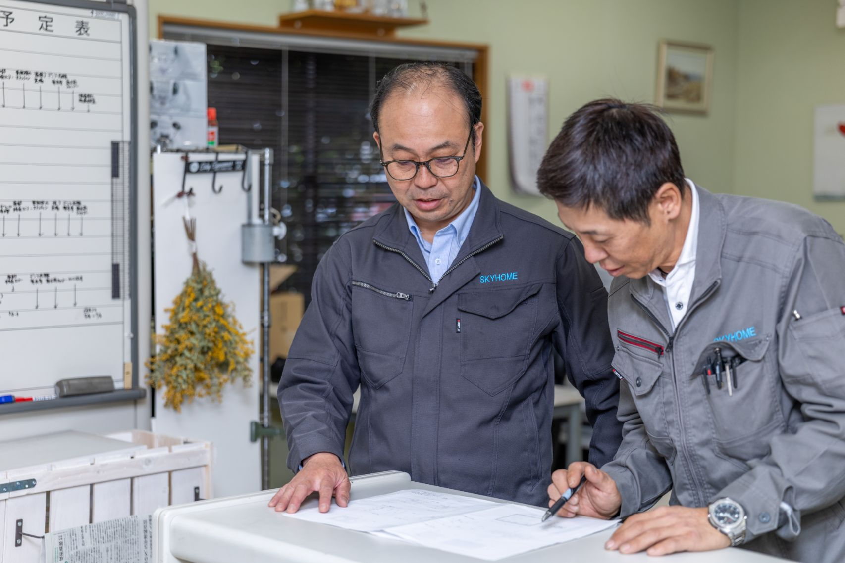 オフィスにて、社長が若い社員に図面を指し示しながら、優しく指導・確認し合っている様子