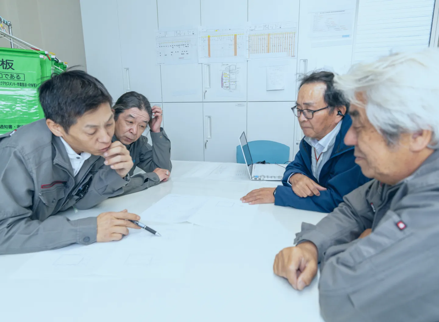 現場で前方を指差し、図面を手にしながらお互いに確認し合う3人の社員たち