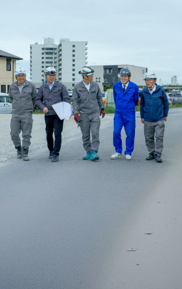 青空の下、笑顔で並んで前を向いて歩く、作業着姿のスカイホームの社員たち