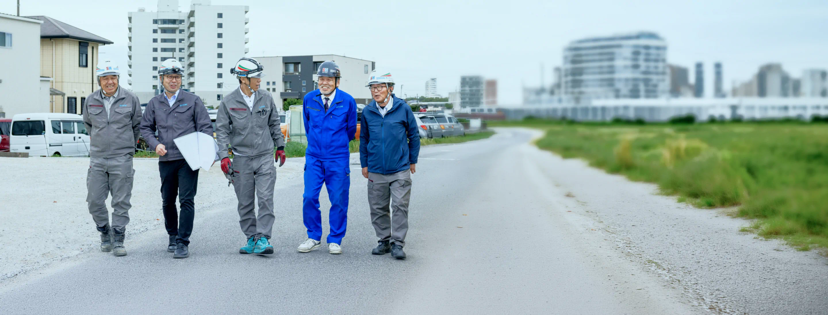 青空の下、笑顔で並んで前を向いて歩く、作業着姿のスカイホームの社員たち