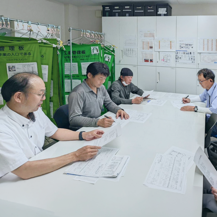 改修現場の屋外で、車両の前で指を差し確認し合いながら最適な工法を相談する社員たち